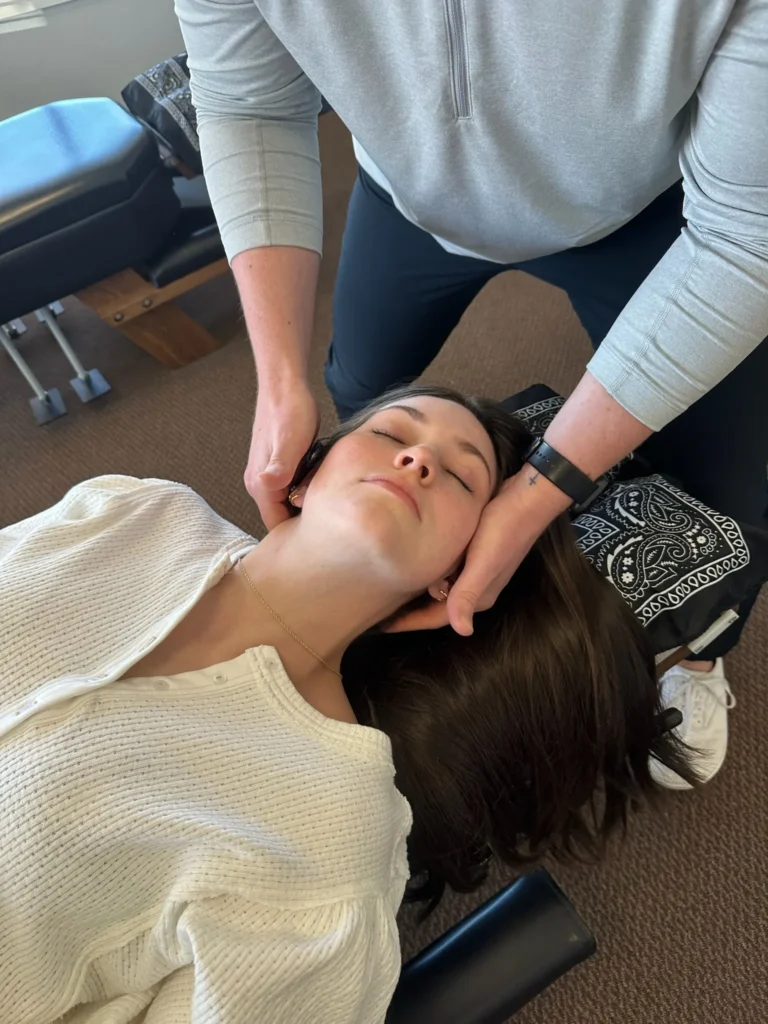 Chiropractor gently adjusting a woman's neck while she lies on a treatment table.