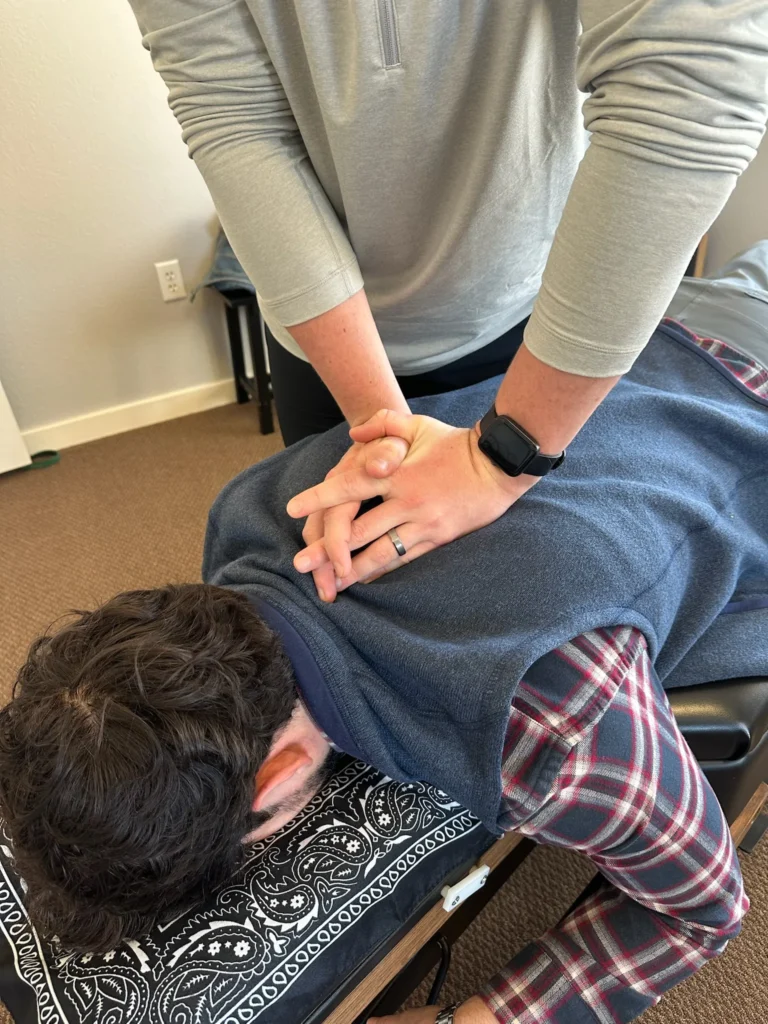 Chiropractor with hands positioned on a man's upper back to perform a spinal adjustment on a treatment table.