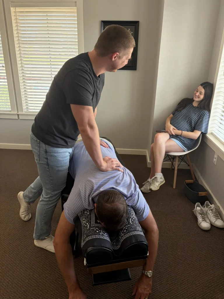 Dr. Cameron Williams performs a spinal adjustment on a patient lying face down while a woman sits nearby.