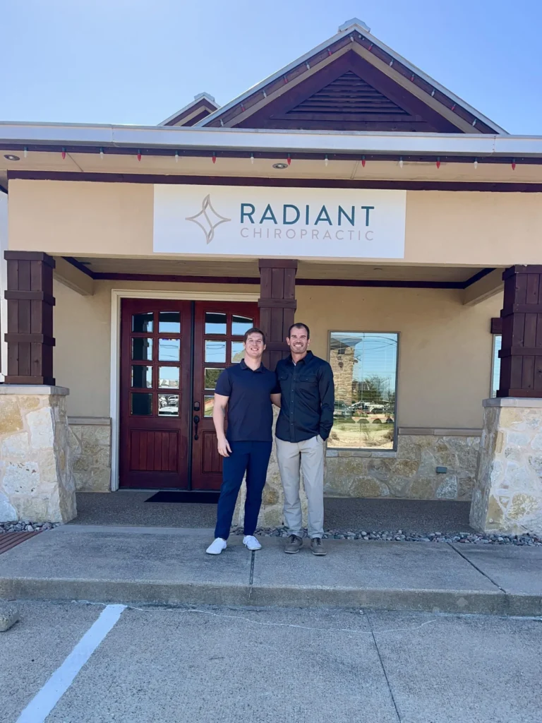 Dr. Cameron Williams stands smiling outside Radiant Chiropractic entrance alongside another man.