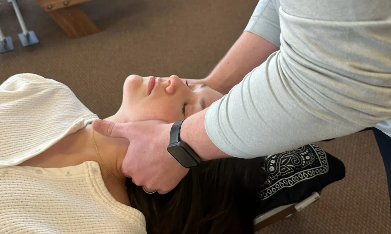Chiropractor performing a cervical spine adjustment on a woman lying supine on a treatment table.