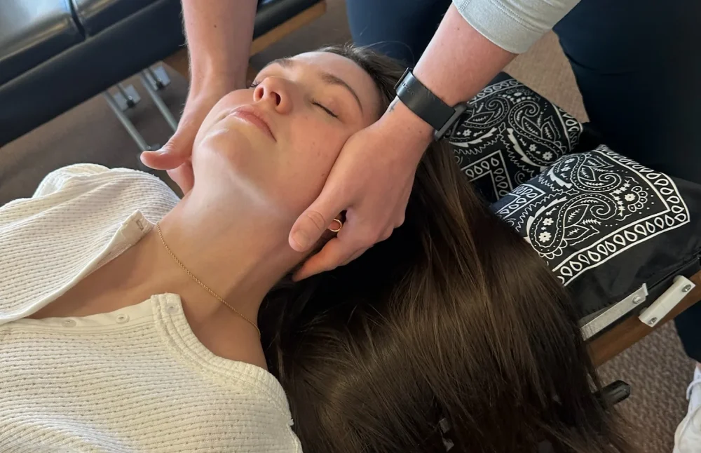 Chiropractor performing a gentle cervical neck adjustment on a woman resting face up on an adjusting table.
