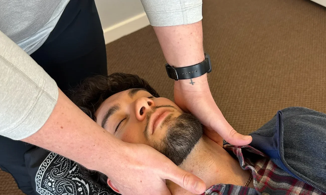 Chiropractor with hands positioned to adjust the neck of a man lying on a treatment table.