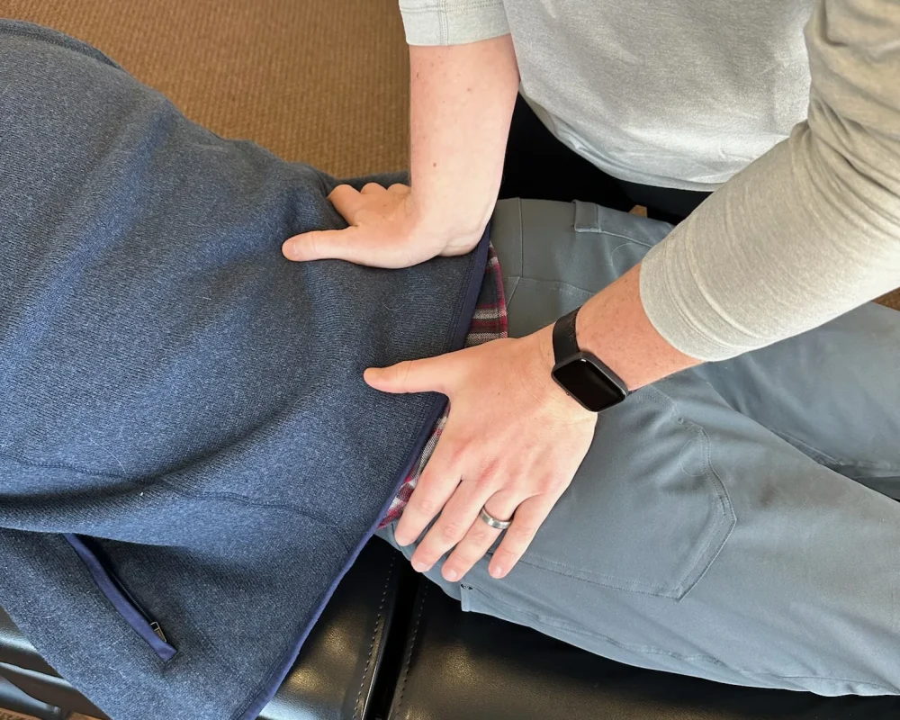 Chiropractor placing hands on a patient's lower back and pelvis during a prone adjustment.
