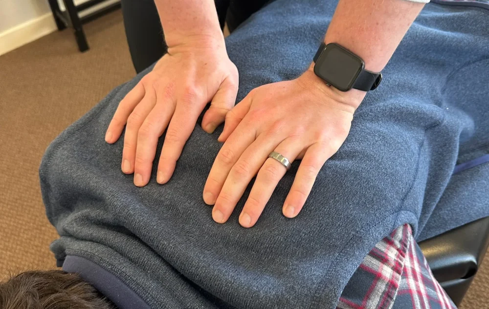 Chiropractor placing both hands on the upper back of a patient lying prone on a chiropractic table.
