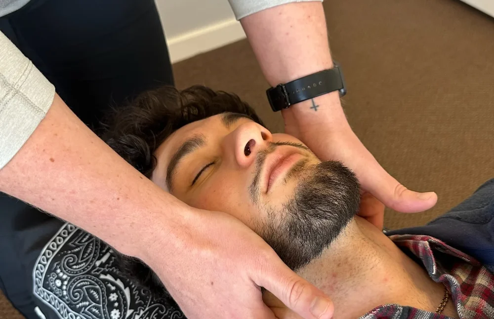 Chiropractor with hands placed on the neck of a man lying face-up on an adjustment table.