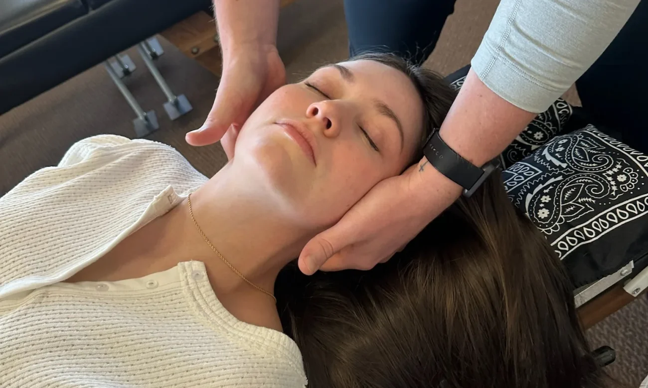 A chiropractor gently palpates and adjusts a woman's cervical spine as she lies face-up on a treatment table.