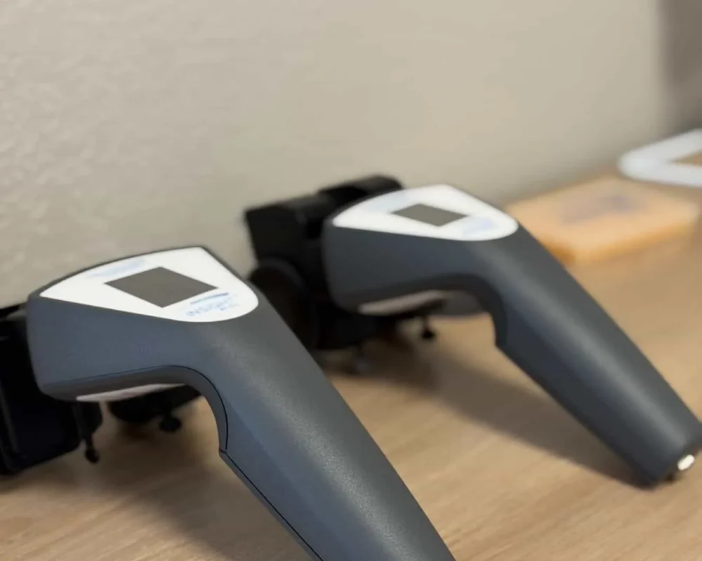 Two CLA INSiGHT scanning devices resting in charging docks on a wooden counter in a chiropractic office.