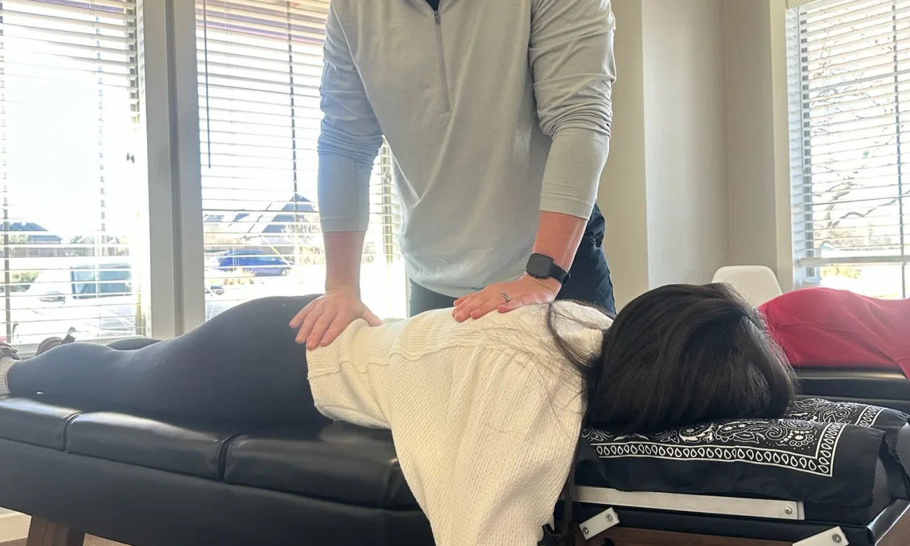 Dr. Cameron Williams assesses a patient's back while she lies face down on a chiropractic adjustment table.