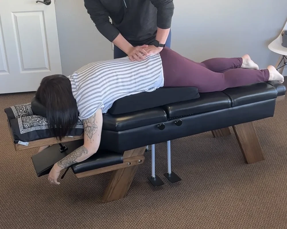 Dr. Cameron Williams adjusts a patient resting prone on a pregnancy support cushion on an adjustment table.