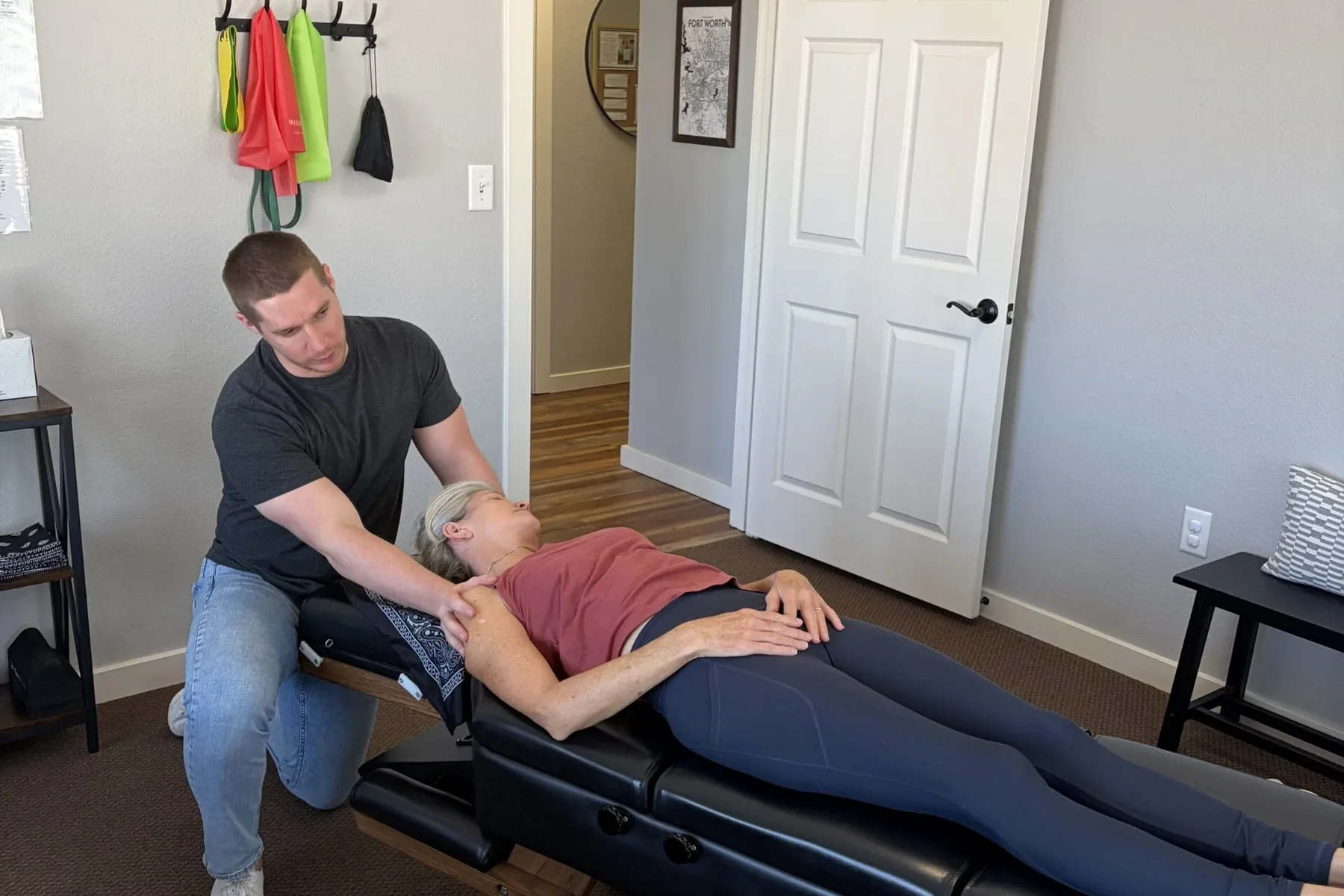 Dr. Cameron Williams examines a patient's shoulder and neck while she lies on a chiropractic adjustment table.