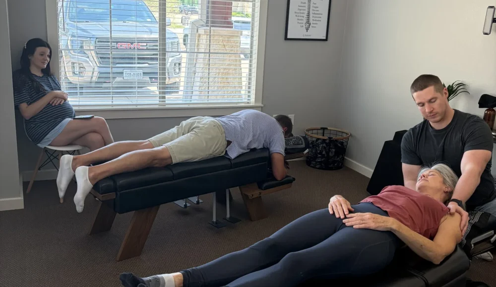 Dr. Cameron Williams adjusts a patient's shoulders at an adjusting table in an open chiropractic room.