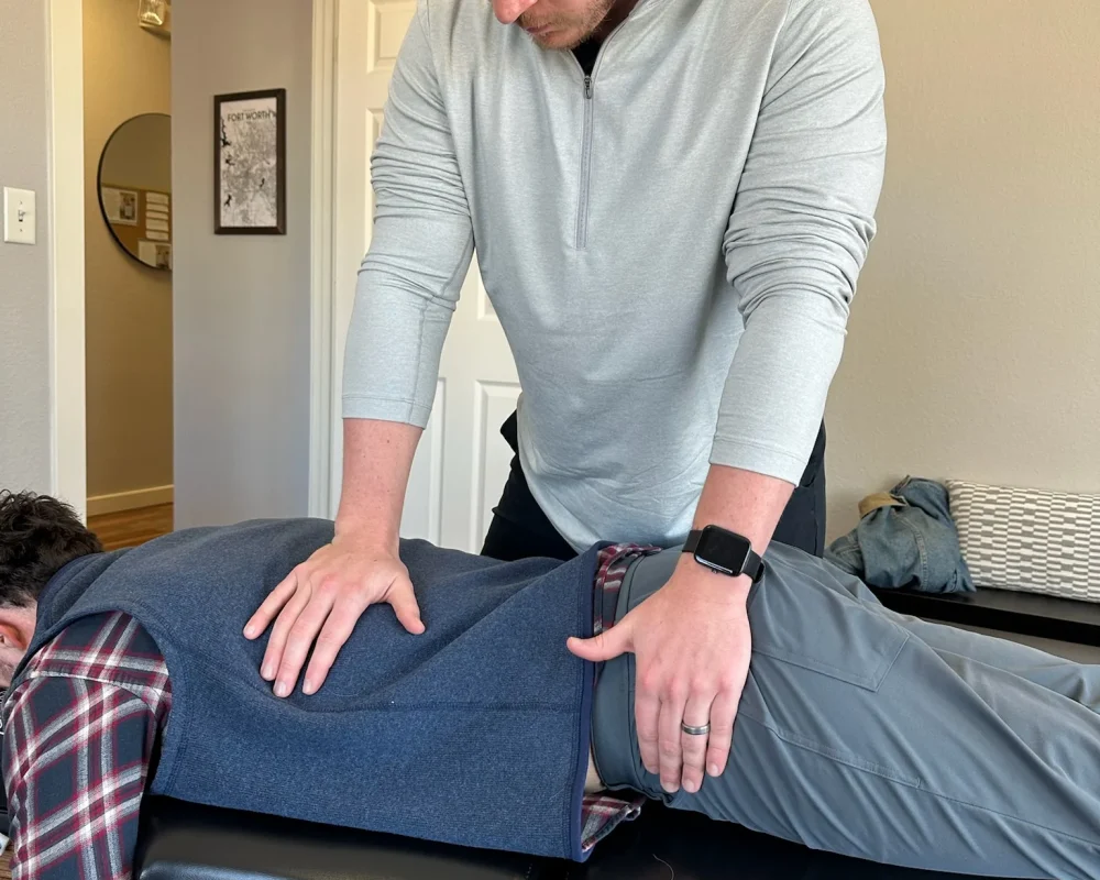 Dr. Cameron Williams places his hands on a patient's back and pelvis during a prone adjustment.