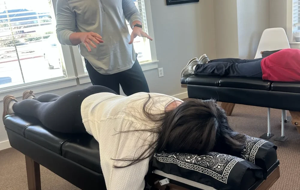 Dr. Cameron Williams speaking with a patient lying face down on an adjusting table in a clinic.