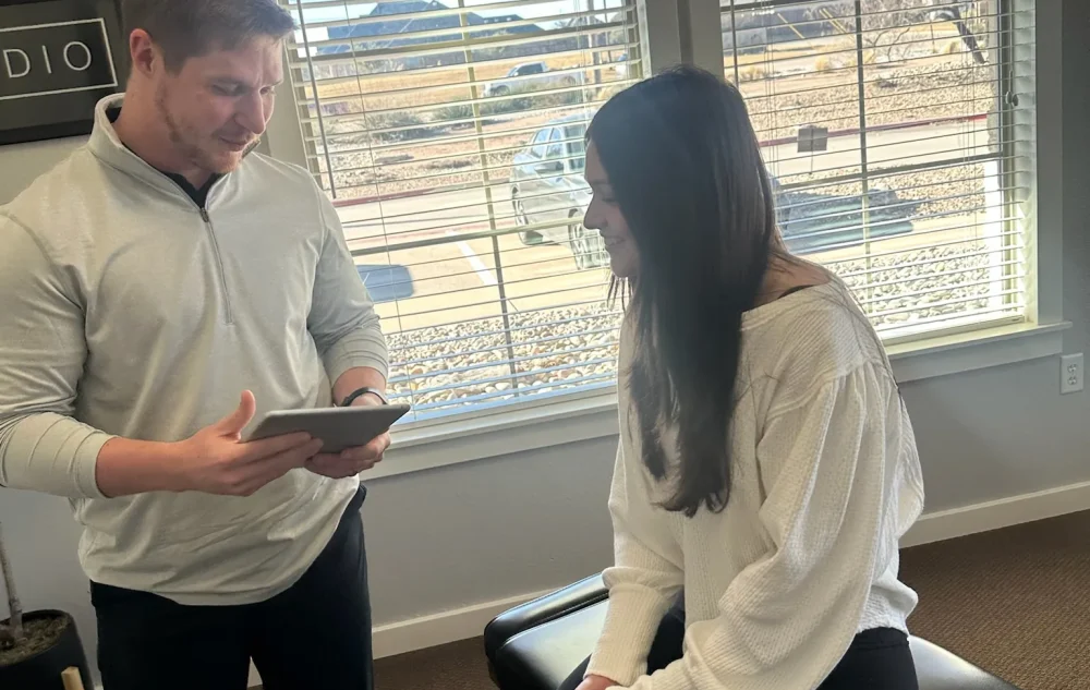 Dr. Cameron Williams holds a tablet while consulting with a patient seated on an adjustment table.