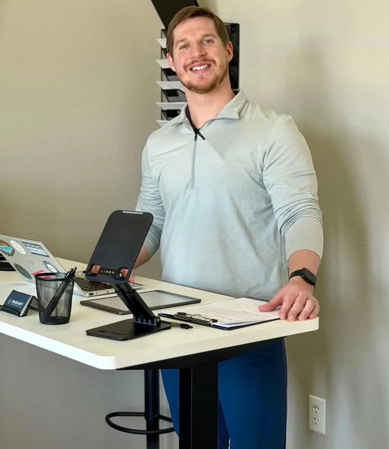 Dr. Cameron Williams smiling while standing behind an office desk with paperwork and a tablet.