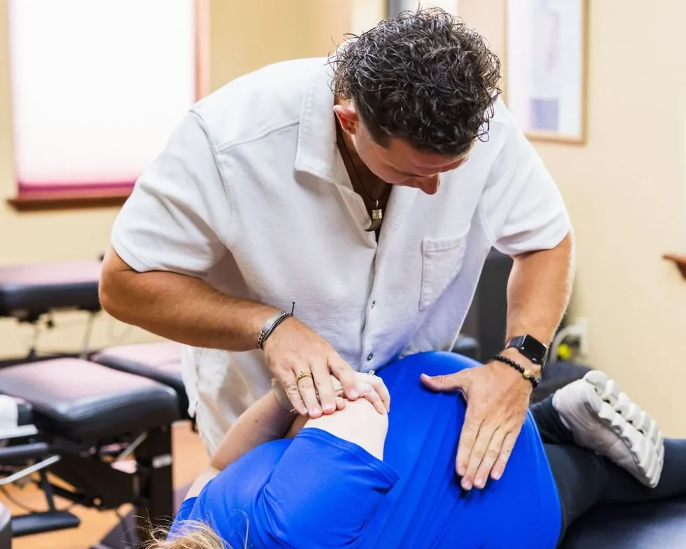 A chiropractor performs a side-posture adjustment on a pregnant woman on an adjusting table.