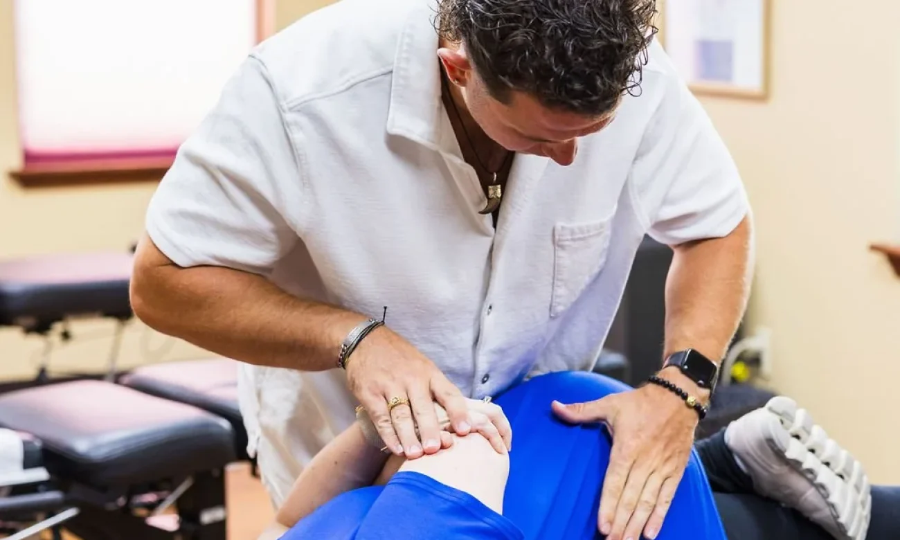 A chiropractor performs a side-posture adjustment on a pregnant woman on an adjusting table.