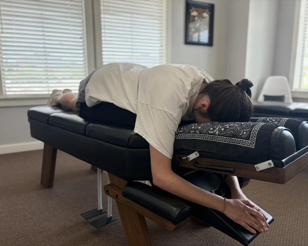 A woman lying face down on a chiropractic adjusting table with a supportive cushion under her midsection.