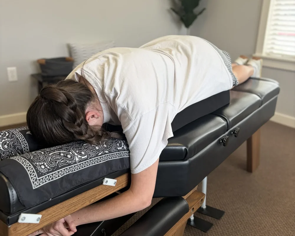 Woman lying face down on a chiropractic adjusting table supported by a specialized pregnancy pillow.